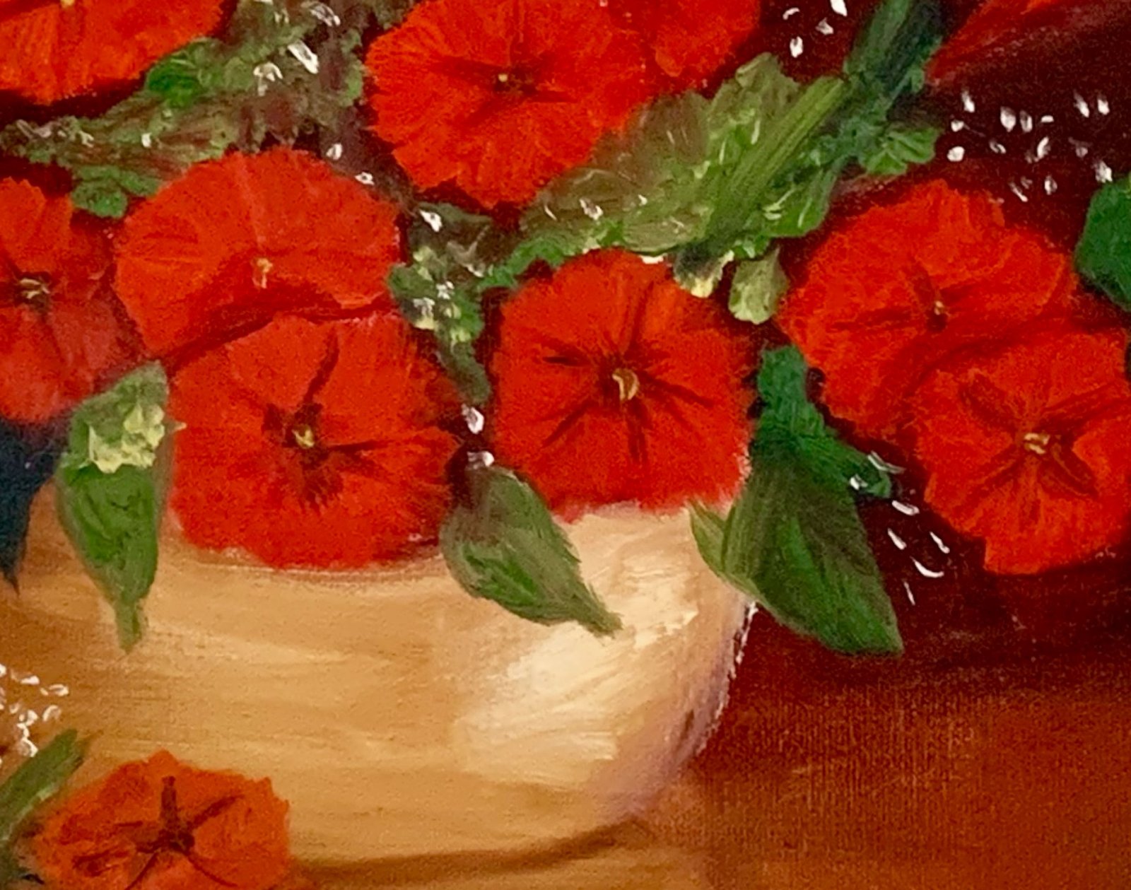 A person with long hair and a beard smiling in front of a wall with a framed painting of red flowers in a vase.